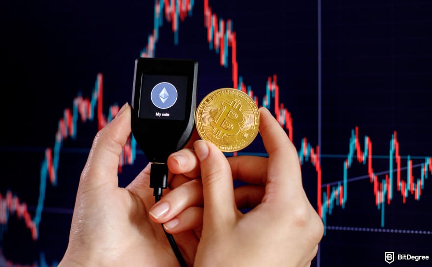 Hardware crypto wallet: a person holding a Trezor wallet and Bitcoin next to price charts.